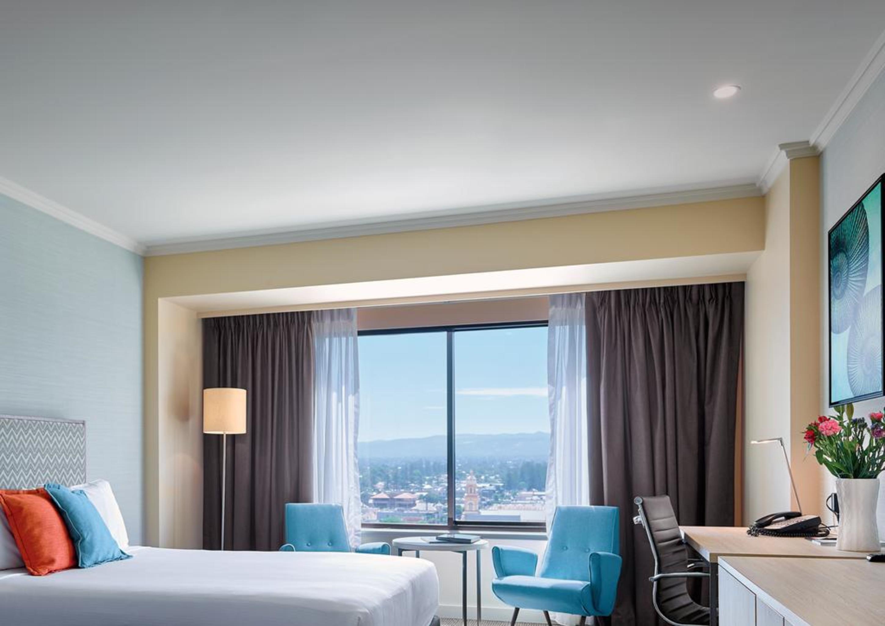 Готель Stamford Grand Adelaide Ґленелґ Екстер'єр фото The photo shows a modern hotel room featuring a queen-sized bed with white linens and colorful decorative pillows. There are two blue chairs beside a small table positioned near a large window that provides a view of the outside, with sheer and dark 