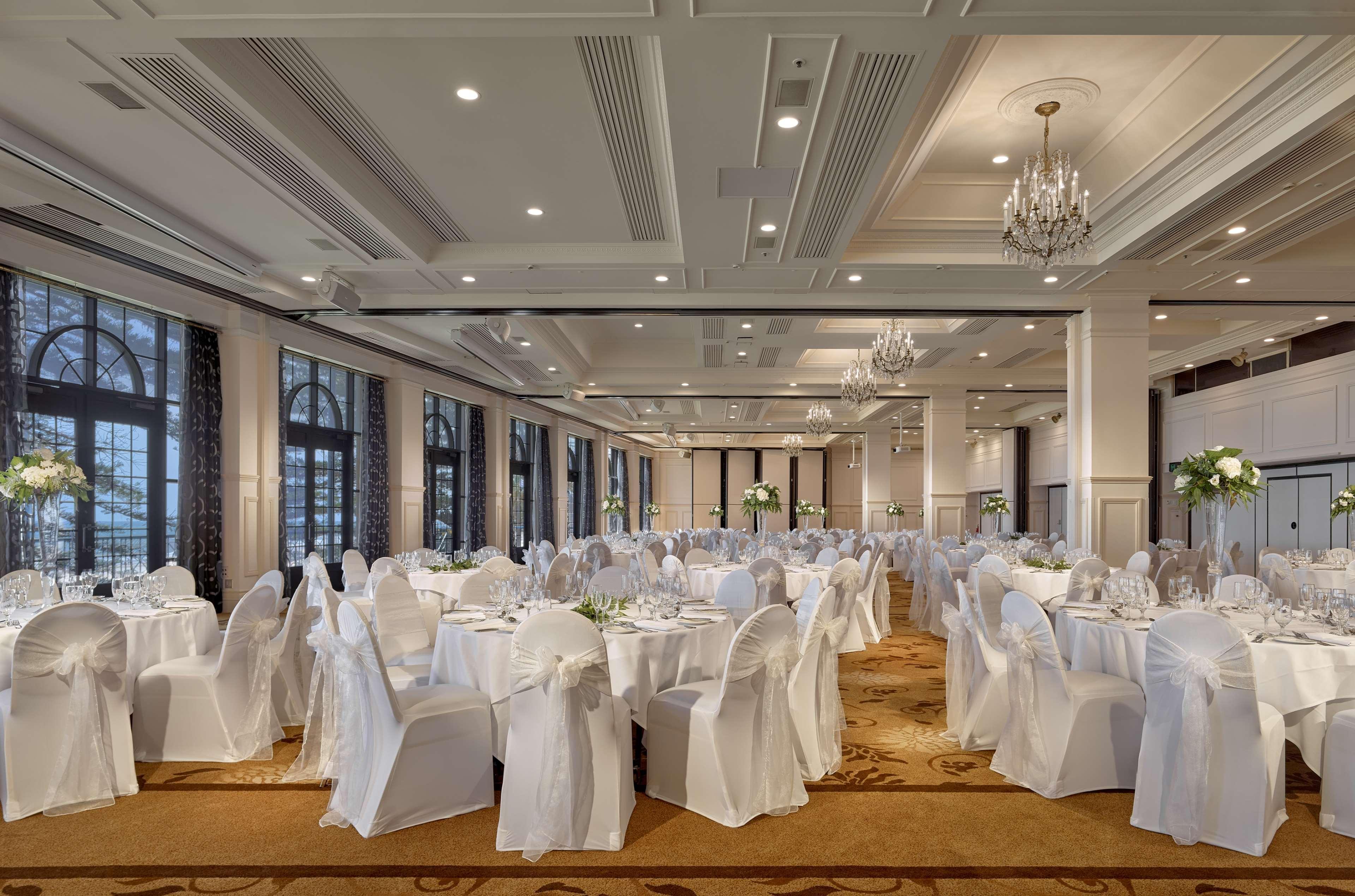 Готель Stamford Grand Adelaide Ґленелґ Екстер'єр фото The photo depicts an elegantly arranged banquet hall or dining area. The space features multiple round tables, each set with white tablecloths and decorated with floral centerpieces. The chairs are covered in white fabric, contributing to a formal at