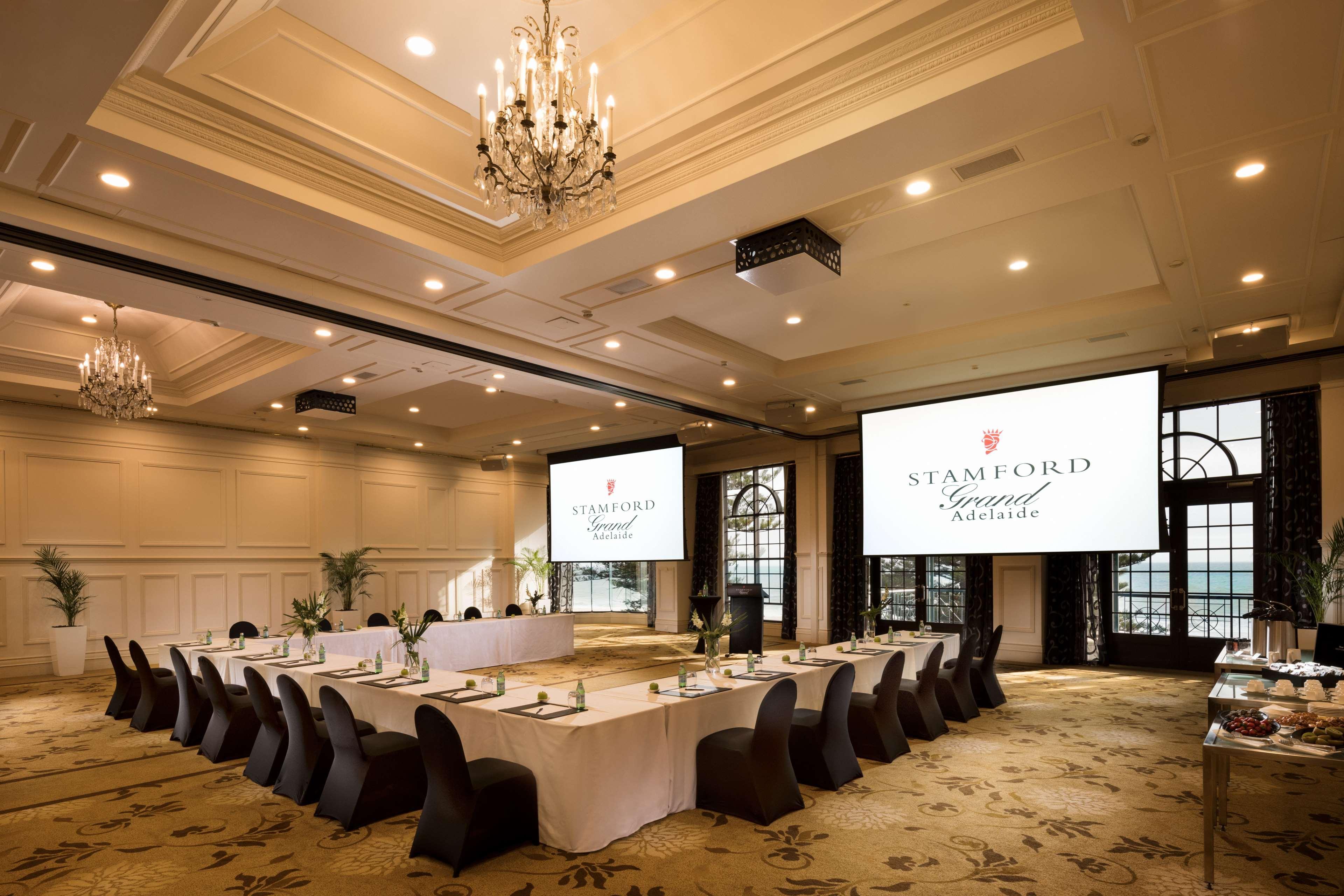Готель Stamford Grand Adelaide Ґленелґ Екстер'єр фото The photo shows a spacious and elegantly designed conference room. The room features a long table set for a meeting, surrounded by stylish chairs. Two large screens are positioned at the front, displaying the logo "Stamford Grand Melbourne." The ceil