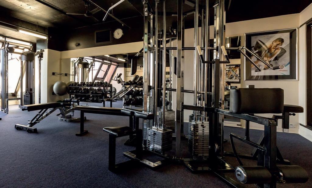 Готель Stamford Grand Adelaide Ґленелґ Екстер'єр фото The photo shows a gym interior with several pieces of exercise equipment. In the foreground, there is a multi-station machine that features various pulleys and weights. To the side, there are benches and free weights, including dumbbells. The gym has